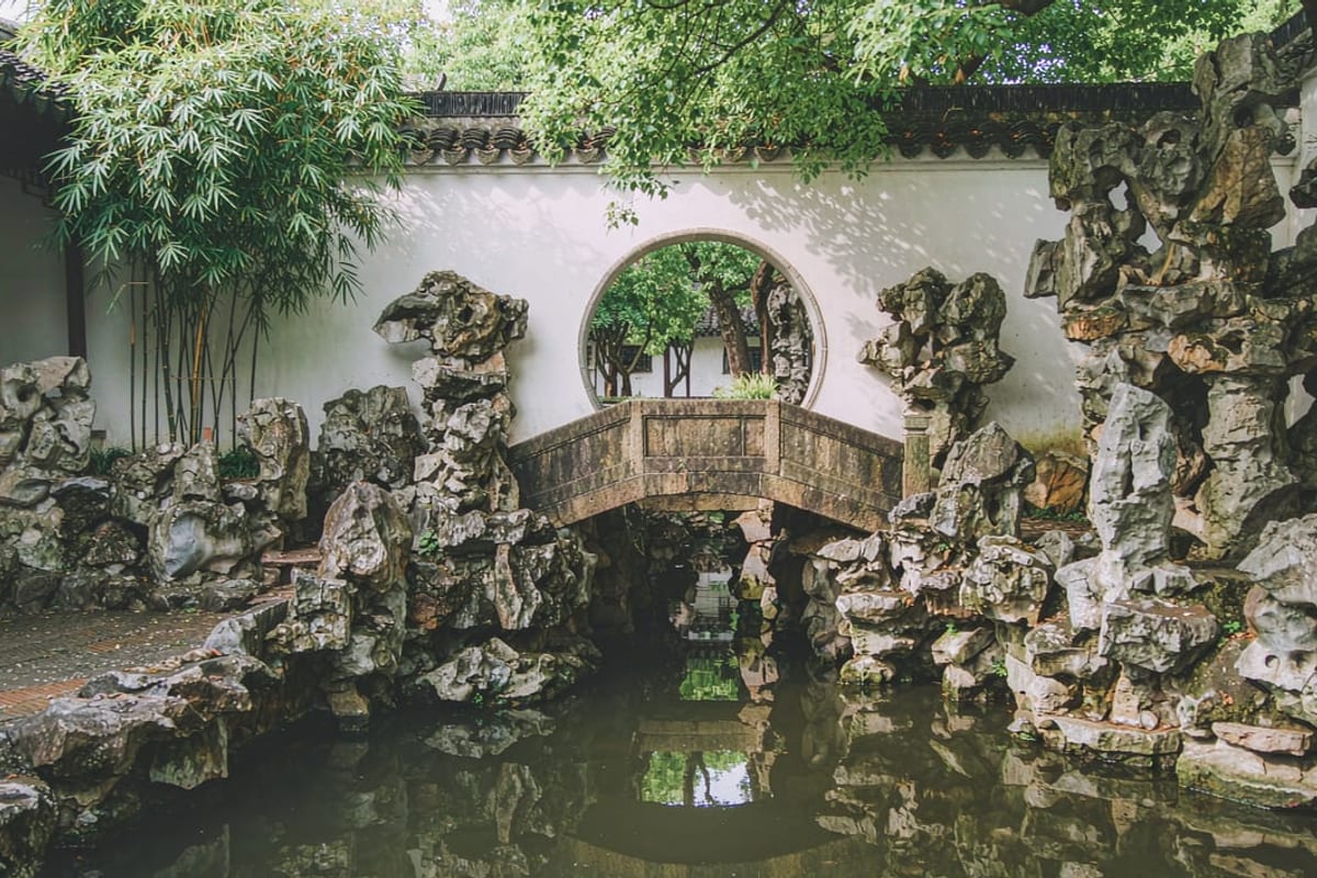 Muro branco com porta circular, ponte de pedra e rochedos num jardim de Suzhou