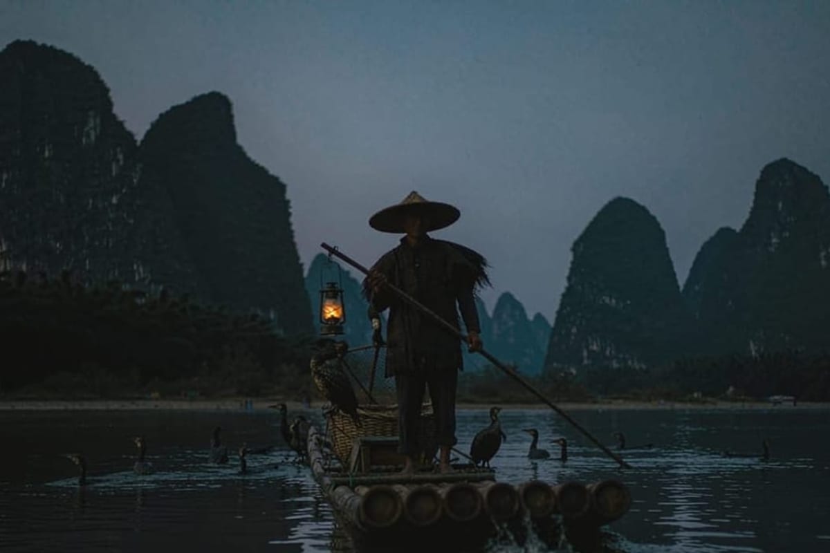 Pescador de cormorões em balsa no rio Li ao entardecer